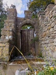 Old stone gateway with wooden door and arched passage, historic landmark with weathered masonry.