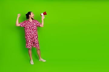 Energetic young man in a stylish pink leopard outfit holding a megaphone and posing lively against a green background
