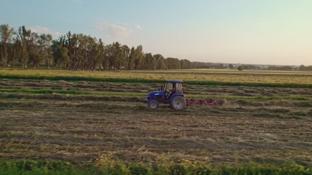 Aerial view of tractor with hay tedders in a field at sunset with golden light.
Tedder for tractor. The machine for gathering hay.