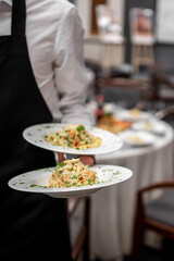 Waiter in black apron serving two plates of gourmet risotto in elegant restaurant setting, showcasing fine dining presentation and hospitality service