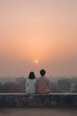 couple sits on old stone wall hand in hand gazing at sunset