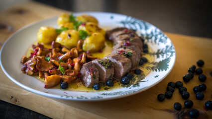 ready to eat and served on a decorative plate - roasted filet from venison, chanterelles and potatoes with fresh herbs out the garden 