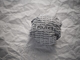 Crumpled paper ball with words Politics on a crumpled white paper background.