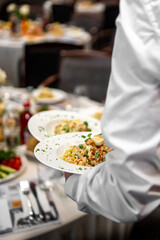 Waiter holding two plates with gourmet salad and boiled eggs at a formal dining event. Elegant table setting in background. Catering service in upscale restaurant or banquet.