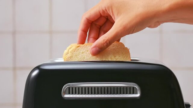 Hand putting bread slices into metal toaster in bright kitchen