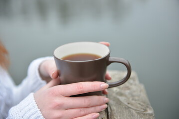 hands holding a brown cup of tea in an autumn park