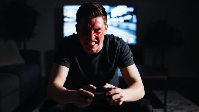 Furious young gamer shouting at screen intensely playing a competitive video game in a dark room Overwhelmed male player showing intense emotion and losing cont