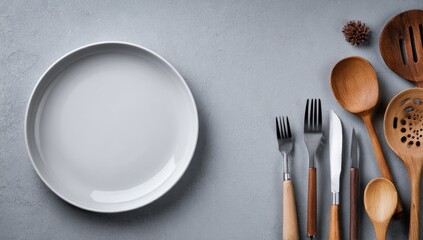 Empty gray plate, wooden & metal kitchen utensils on a gray background