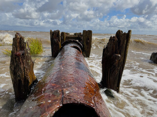 Rusty outfall pipe leading into sea with waves crashing, dramatic maritime coastal scene.