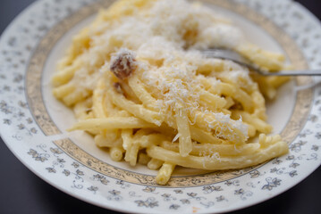 On a black table in a white plate, spaghetti with the so-called Carbonara sauce, which contains bacon, garlic, sour cream, egg, and sliced ​​Parmesan cheese. Delicious
