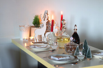 Table set for Christmas meal, with plates, wine, decorations and lit candles. Selective focus.