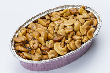 Caramel toffee cake cashew nuts in foil container, sweet dessert, baked snack, nut topping, delicious treat, isolated on white background