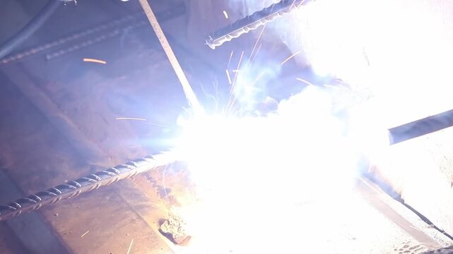 Welding work using electrodes. Welding two bars of reinforcement to create a frame for stairs in the country. Repair and construction work close-up. A person welds metal parts. Flash from welding work