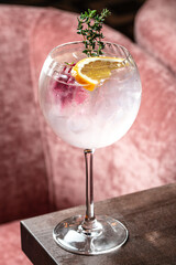 Chilled gin tonic cocktail with lemon slice and herbs in wine glass on wooden table, close up