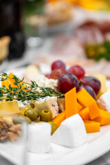 Close-up of assorted cheeses, grapes, olives, walnuts, and herbs on a rustic charcuterie board. Gourmet appetizer for party, catering, or food styling concepts