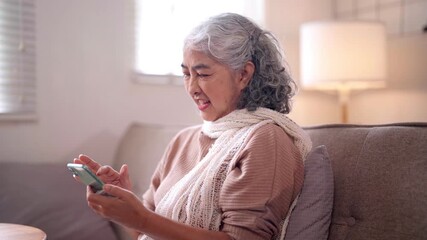 Older Asian woman happily engages smartphone connects family friends online social media technology comfort home living room digital device entertainment - Powered by Adobe
