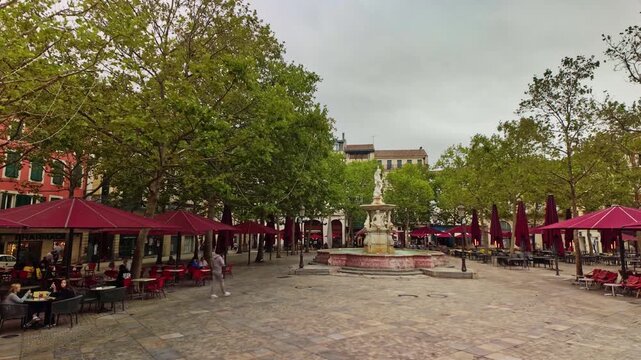 Timelapse sur la place Carnot &agrave; Carcassonne, terrasses rouges anim&eacute;es sous un ciel gris, atmosph&egrave;re urbaine dynamique et contrast&eacute;e en Occitanie.
