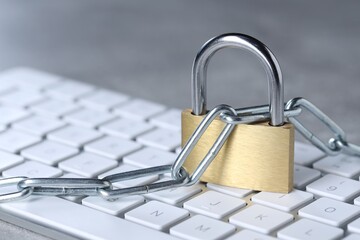Cyber safety. Metal padlock, chain and computer keyboard on grey table, closeup