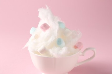 Tasty cotton candy with colorful marshmallows in cup on pink background, closeup