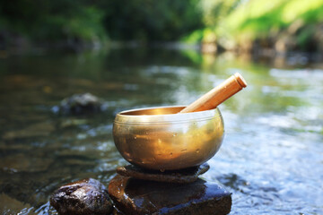 Tibetan singing bowl with mallet on stone near river