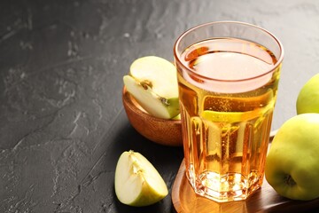 Delicious cider in glass and apples on black table, closeup. Space for text