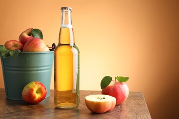 Delicious cider in glass bottle and apples on wooden table against orange gradient background. Space for text