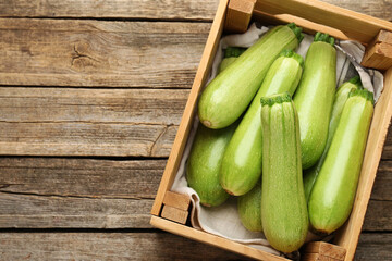 Fresh ripe zucchinis in crate on wooden table, top view. Space for text