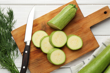 Fresh ripe zucchinis and knife on white wooden table, flat lay