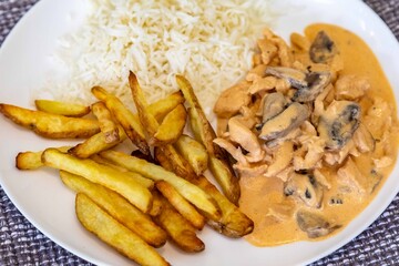 Delicious chicken stroganoff with rice and rustic roasted potatoes on a round white plate and a nice clean table setting