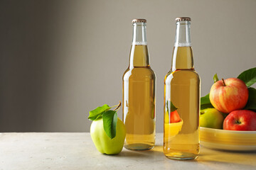Delicious cider in glass bottles and apples on gray table against light background. Space for text