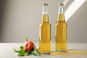 Delicious cider in glass bottles and apples on gray table against light background