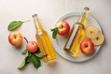 Delicious cider in glass bottles and apples with green leaves on beige table, flat lay