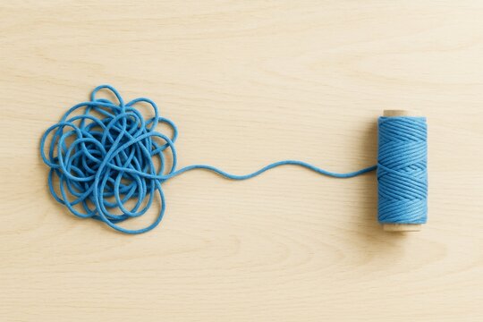 Blue tangled string next to a neatly rolled spool on light wood background, symbolizing chaos and order contrast in minimal style