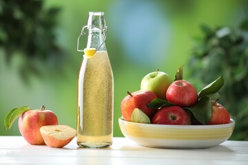 Delicious cider in glass bottle and apples on white wooden table outdoors