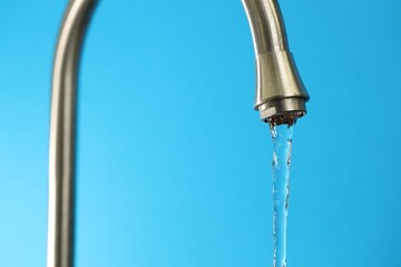 Water saving concept. Stream of water flowing from tap on light blue background, closeup © New Africa