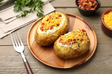 Tasty baked potatoes with sour cream, green onion, cheese and bacon served on wooden table, closeup