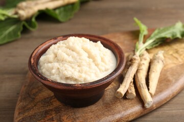 Tasty horseradish sauce and roots on wooden table, closeup