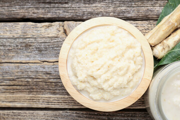 Tasty horseradish sauce and roots on wooden table, flat lay. Space for text
