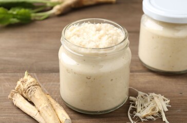 Tasty horseradish sauce and roots on wooden table, closeup