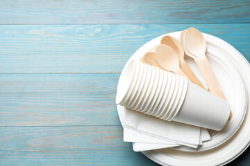 Set of disposable tableware and napkins on light blue wooden table, top view. Space for text