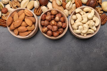 Mix of different nuts in bowls on grey table, flat lay. Space for text