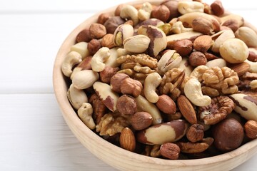 Mix of different nuts in bowl on white wooden table, closeup