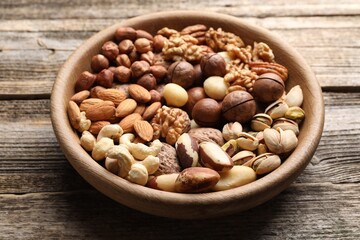 Mix of different nuts in bowl on wooden table, closeup