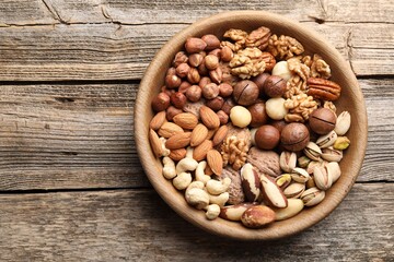 Mix of different nuts in bowl on wooden table, top view. Space for text