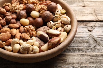 Mix of different nuts in bowl on wooden table, closeup