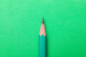 One sharp graphite pencil on green background, top view