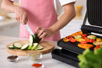 Man cutting zucchini while cooking vegetables on electric grill in kitchen, closeup