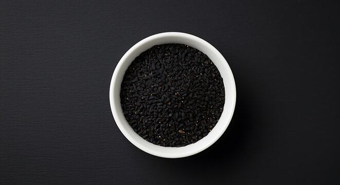 White bowl of black cumin seeds on dark background