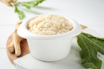 Tasty horseradish sauce and roots on white wooden table, closeup