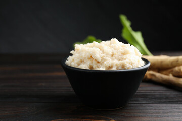 Tasty horseradish sauce and roots on black wooden table, closeup. Space for text